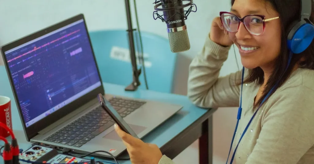 Woman smiling at podcast hosting comparison setup with laptop, microphone, mixer, and headphones in recording studio.