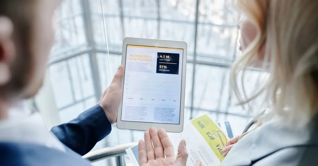 Two people reviewing membership comparison data on tablet with analytics dashboard displayed.