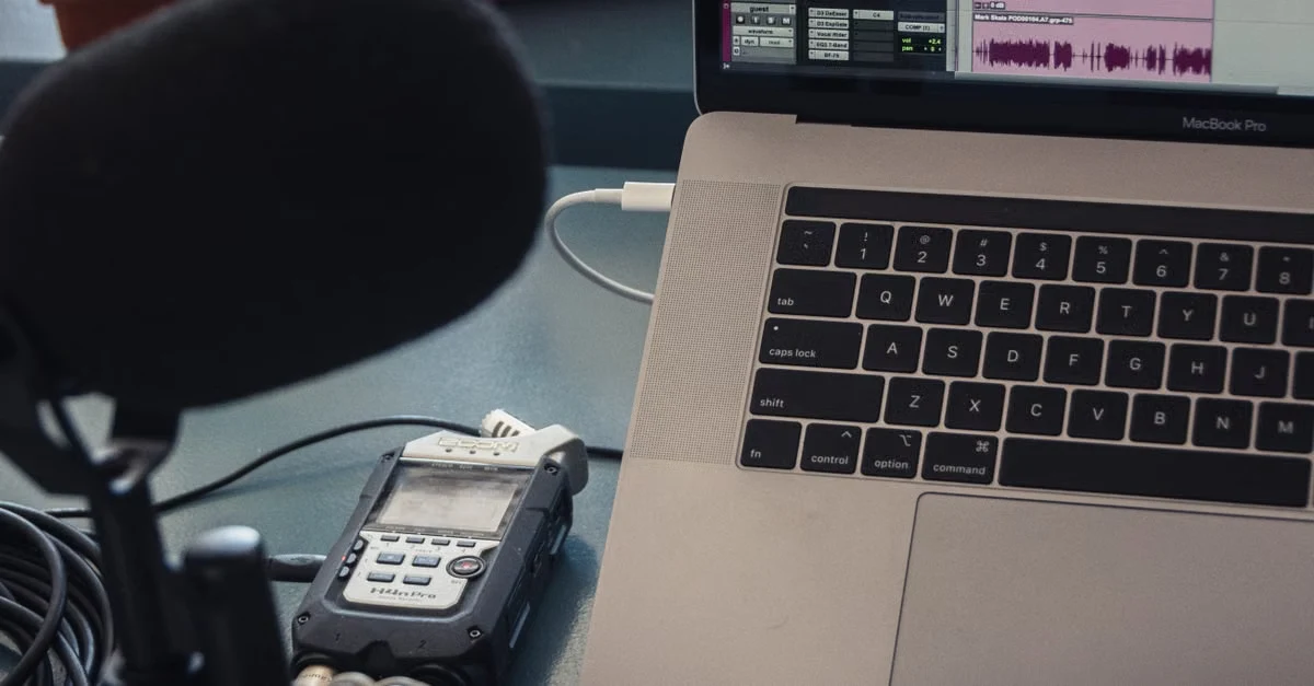 Professional podcast setup with condenser microphone, portable recorder, and laptop displaying audio editing software.