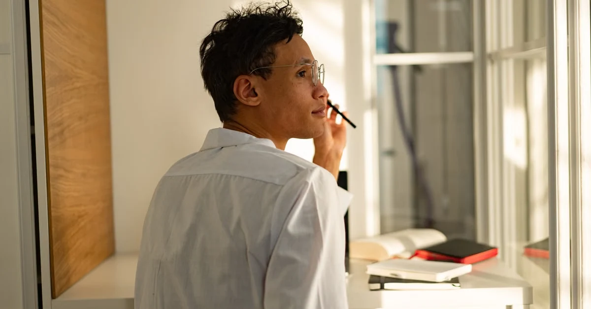 Man in white shirt thoughtfully holding pen at desk, considering private podcast platforms for content distribution.